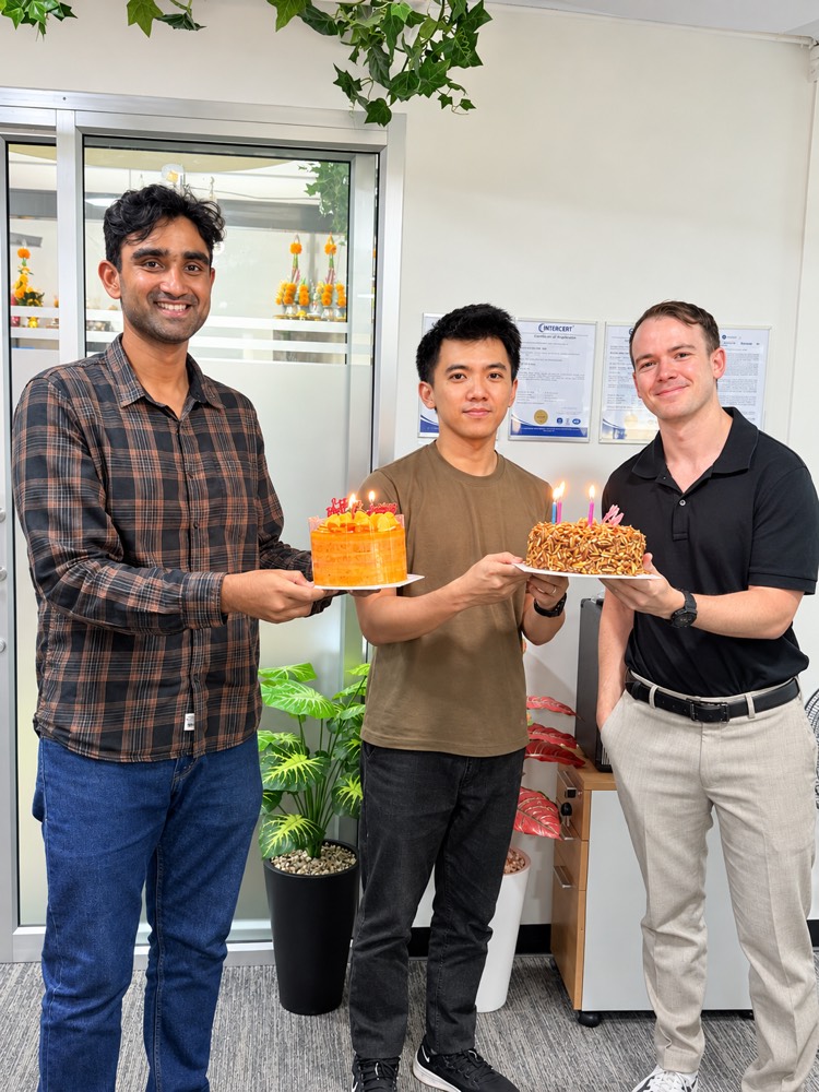 Three teammates in the office holding birthday cakes with lit candles